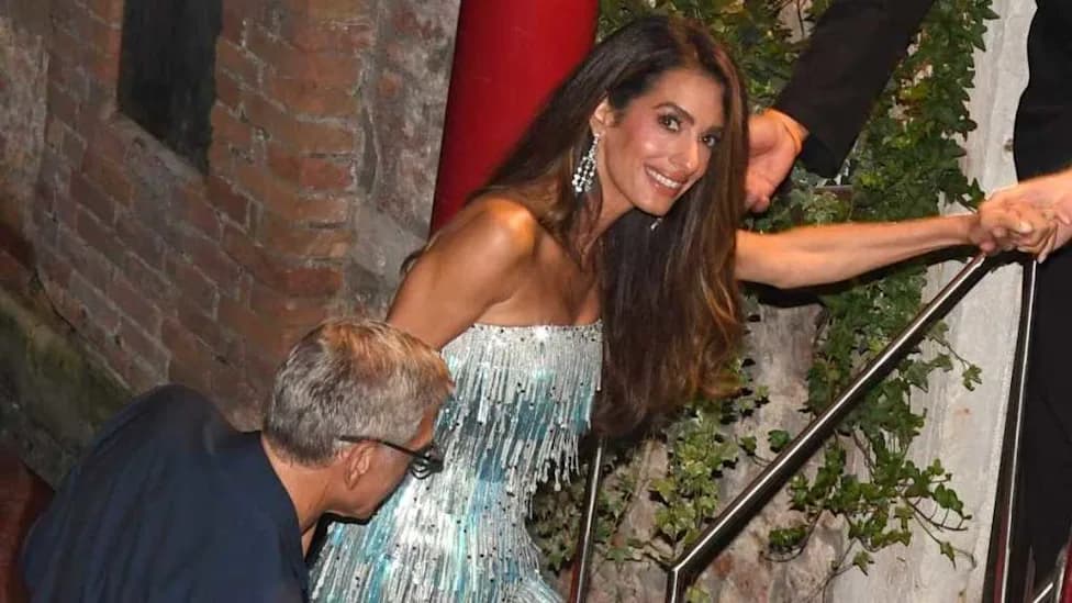 Amal Clooney smiling while walking up stone steps in a sparkling fringe dress