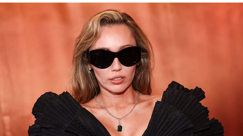 Miley Cyrus wearing sunglasses and a black ruffled dress
