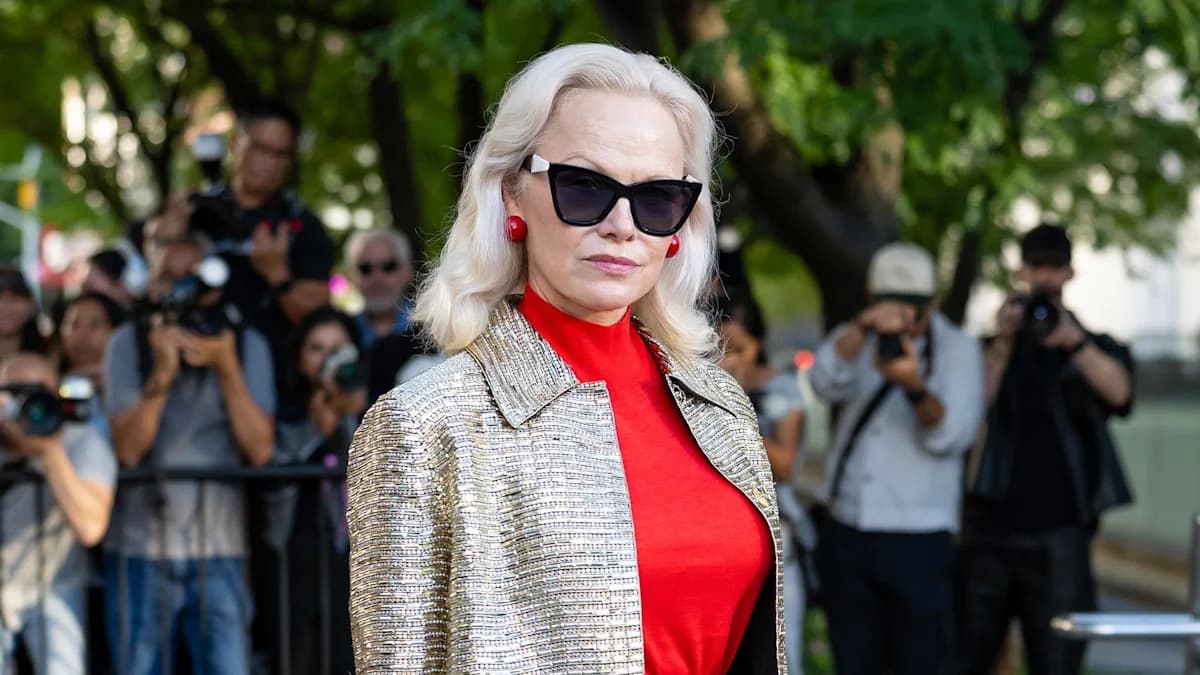 Pamela Anderson wearing a red top and gold jacket at a fashion week event