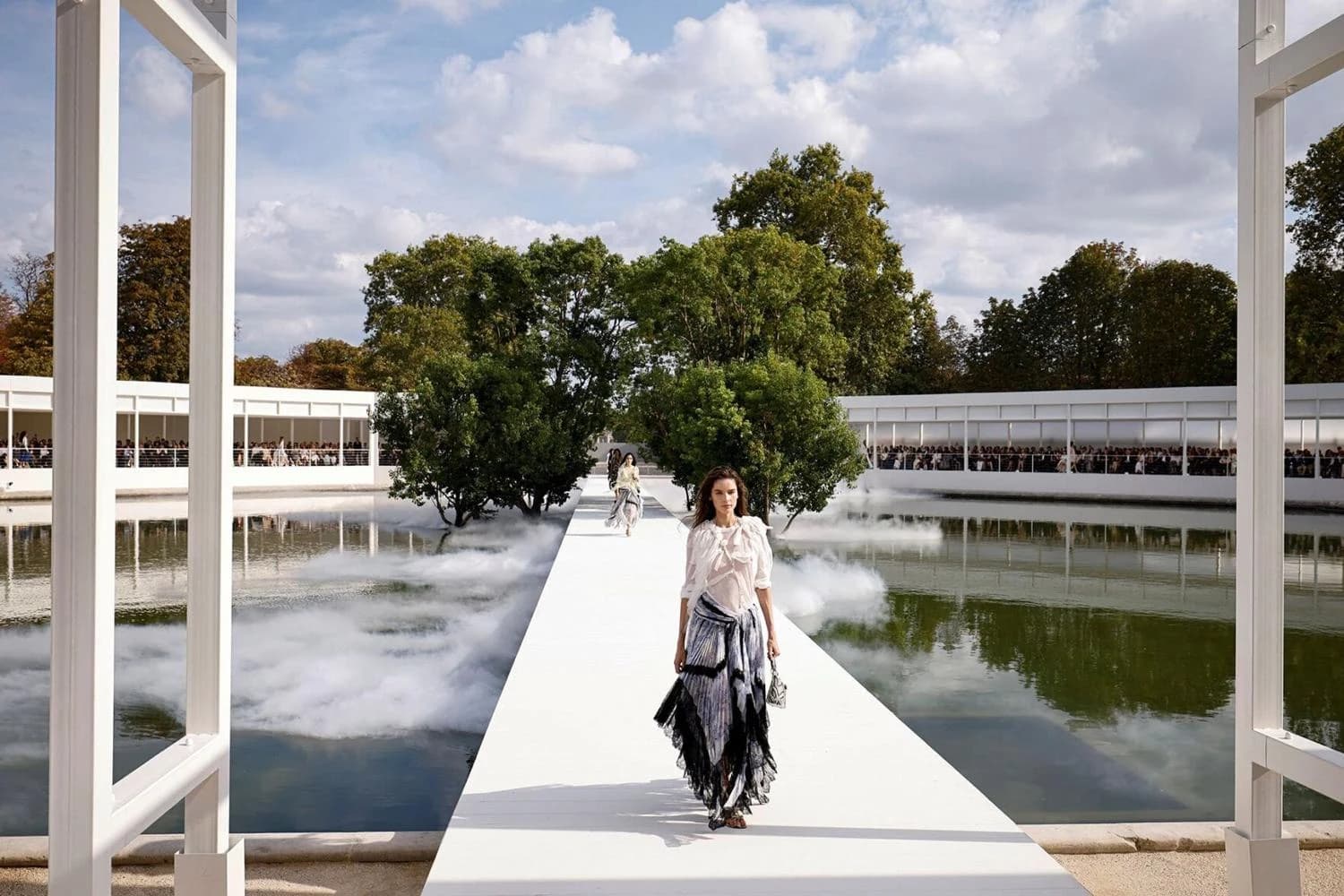 Model walking a runway between reflecting pools at a Paris Fashion Week show