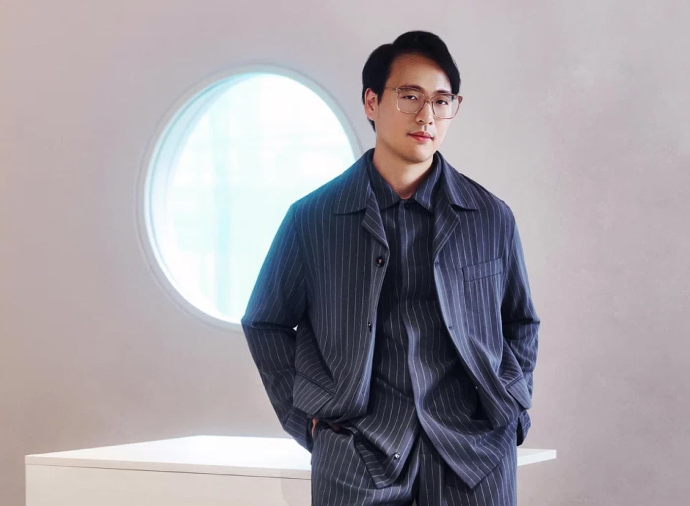Chayadi Karim in a pinstriped jacket standing in front of a round window