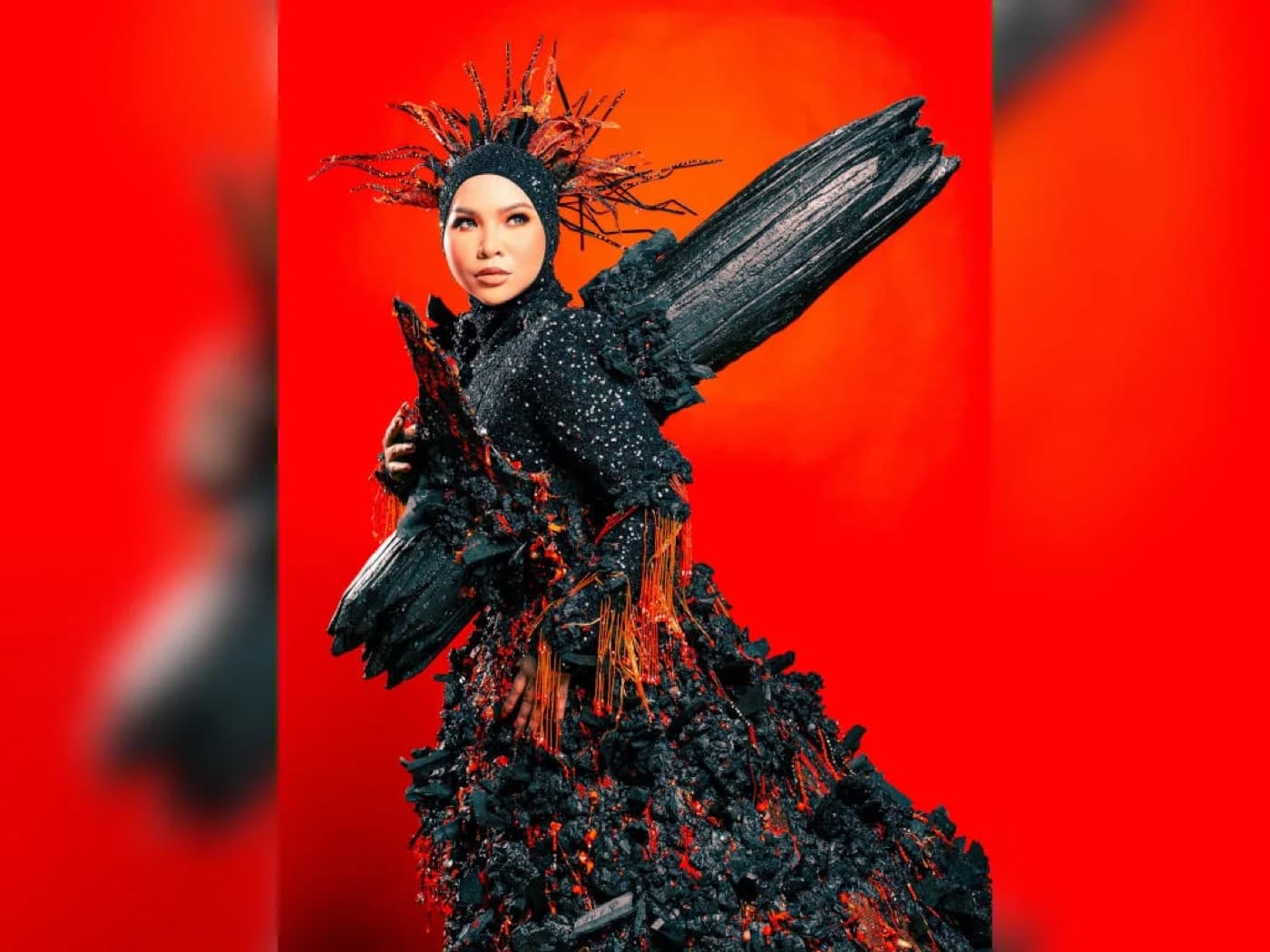 Aina Abdul in a dramatic black volcano themed costume with wing details against a red backdrop