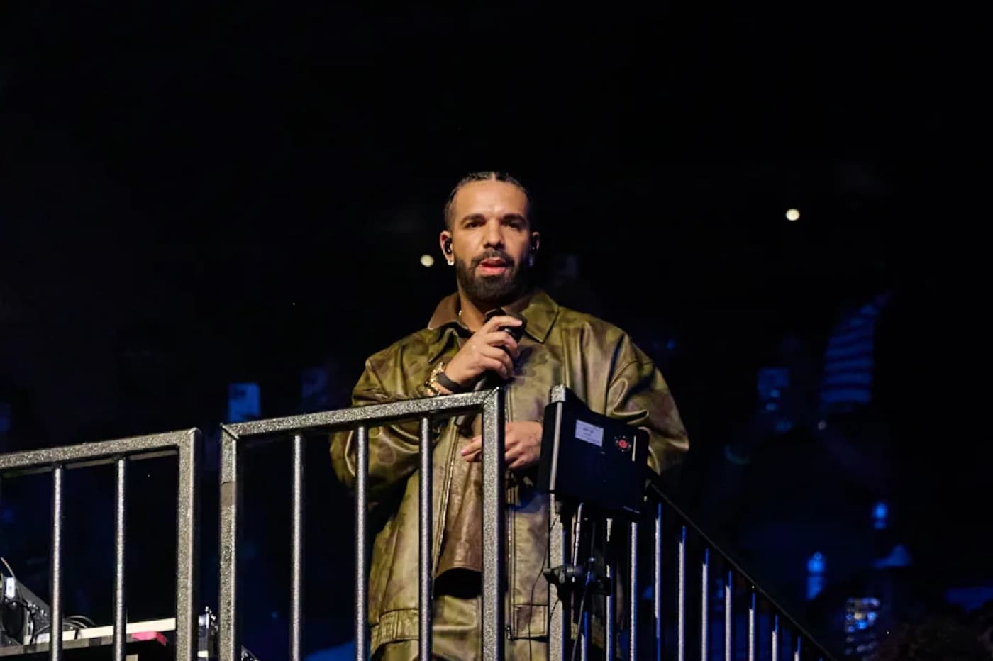Drake performing on stage in a metallic jacket holding a microphone