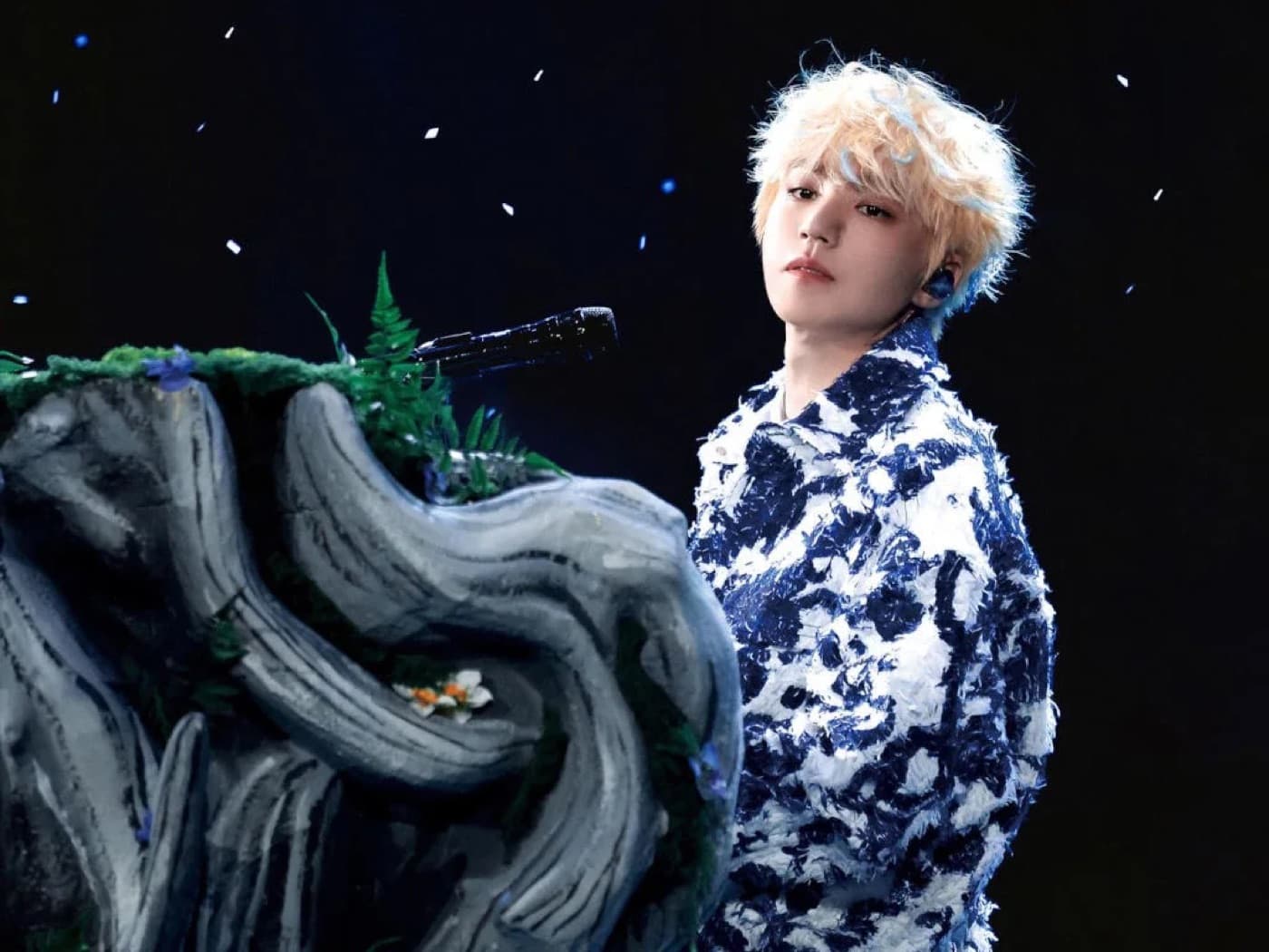 Wang Junkai performing on stage in a blue and white patterned jacket against a night sky backdrop