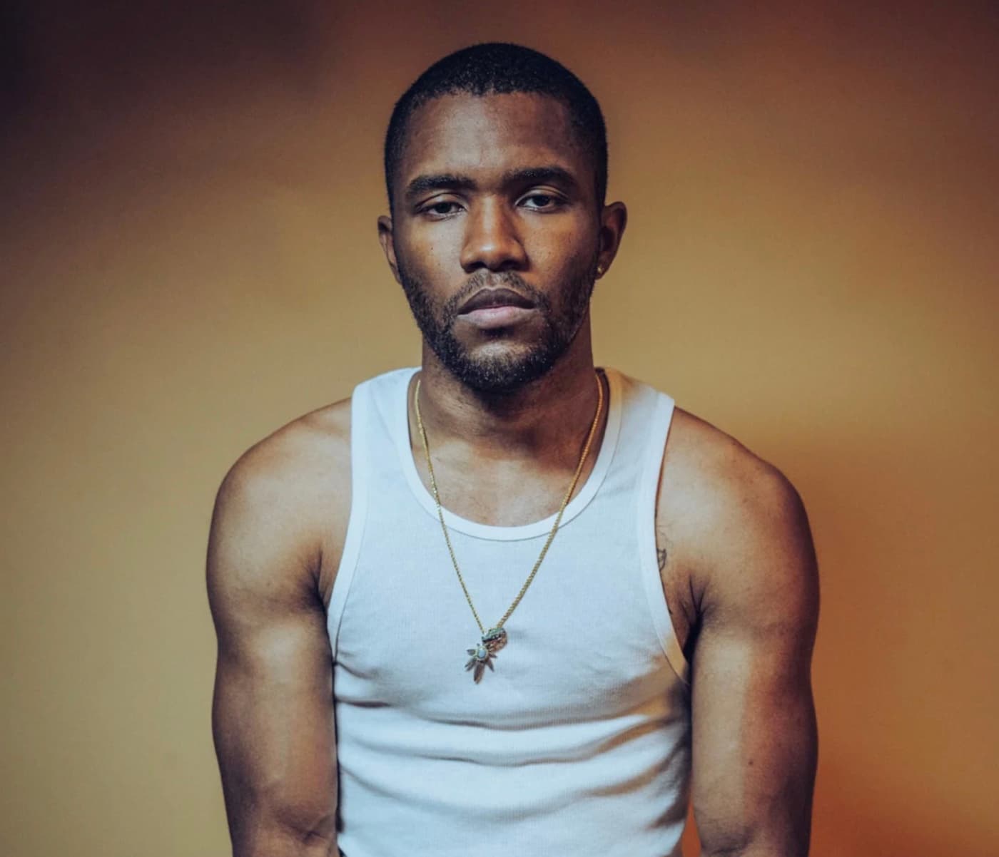 Frank Ocean in a white tank top and gold chain against an amber backdrop