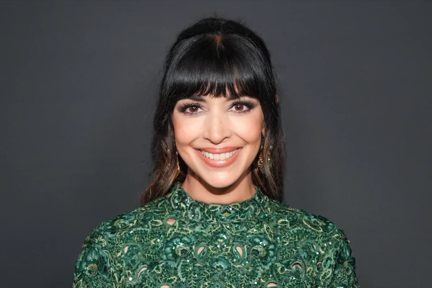 Hannah Simone smiling in an embroidered green top against a dark backdrop
