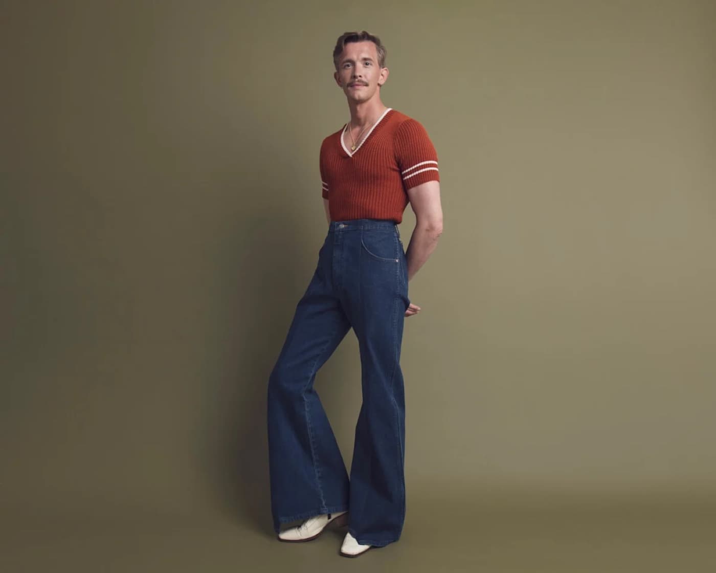 Stephen Libby posing in a burnt orange knit top and flared denim trousers