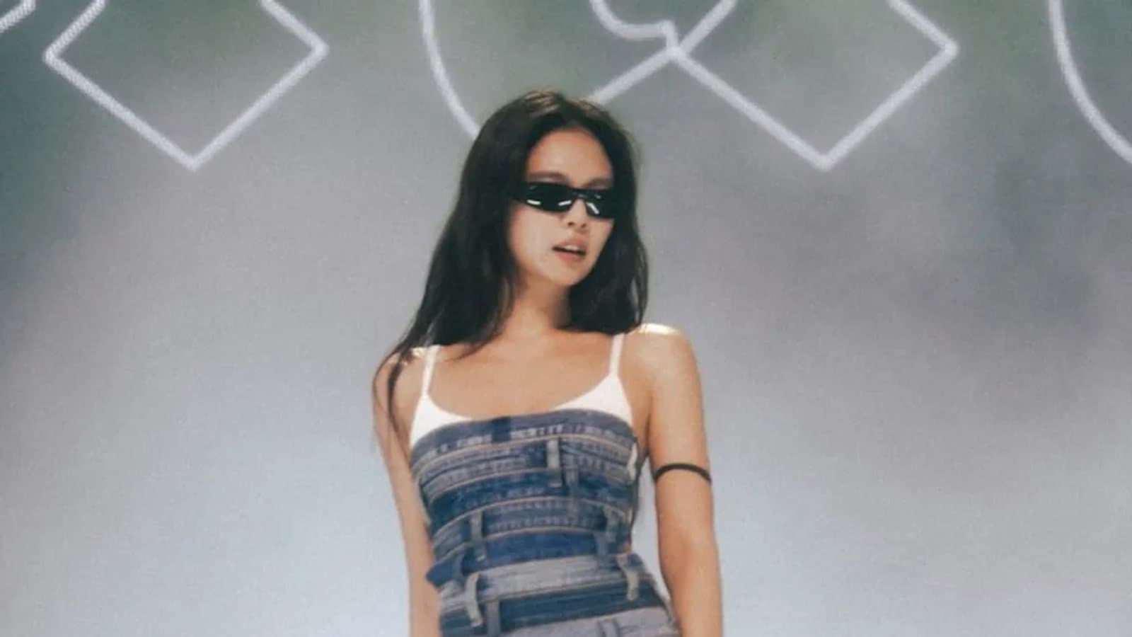 Jennie performing on stage in a denim outfit and sunglasses, backlit by a stage screen.