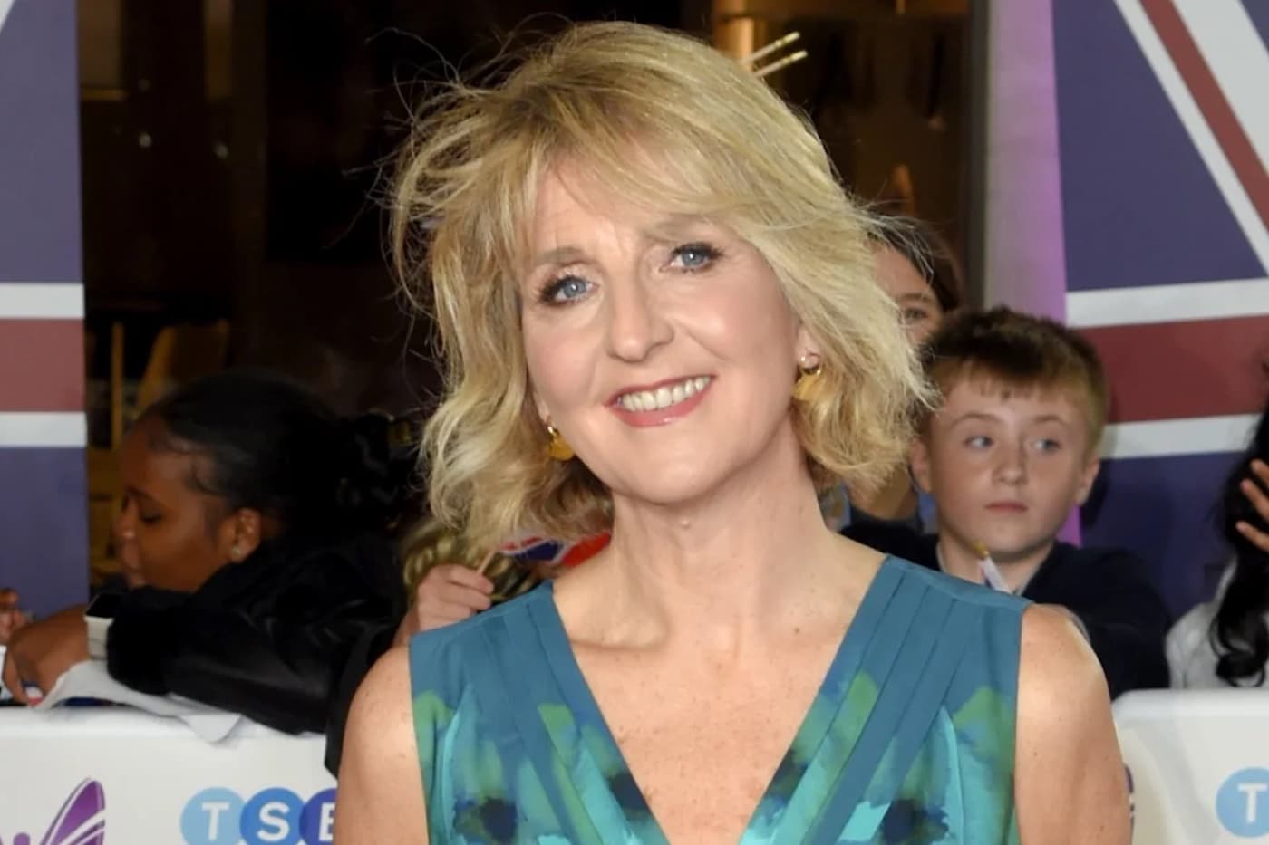 Kaye Adams smiling in a teal dress at a red carpet event