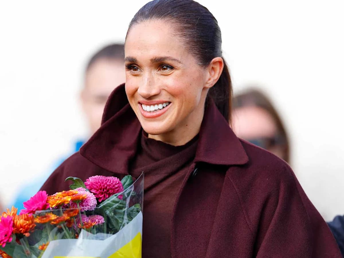 Meghan Markle smiling while holding a bouquet of flowers during a public appearance