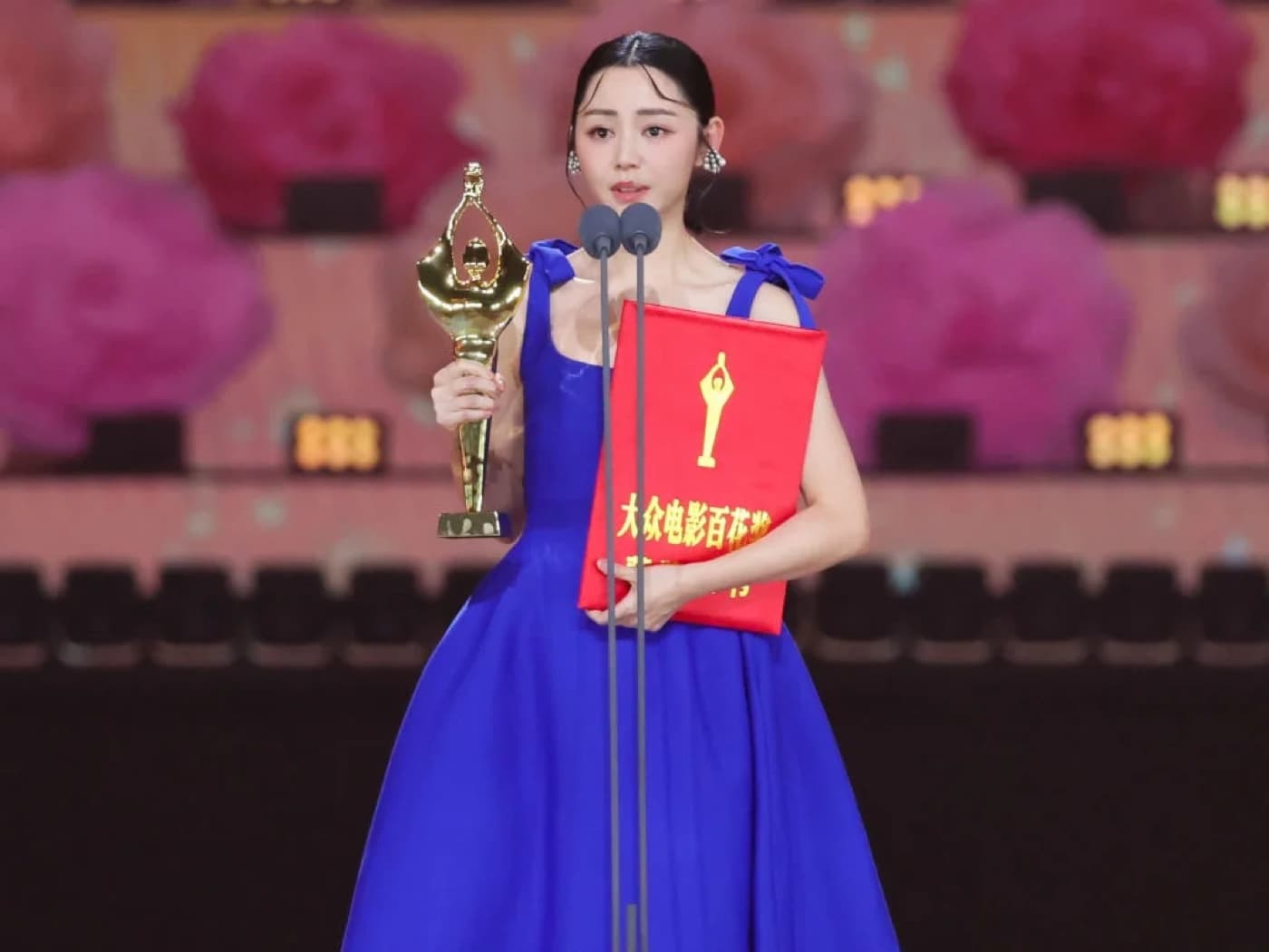 Michelle Wai in a blue gown holding a trophy and red award folder