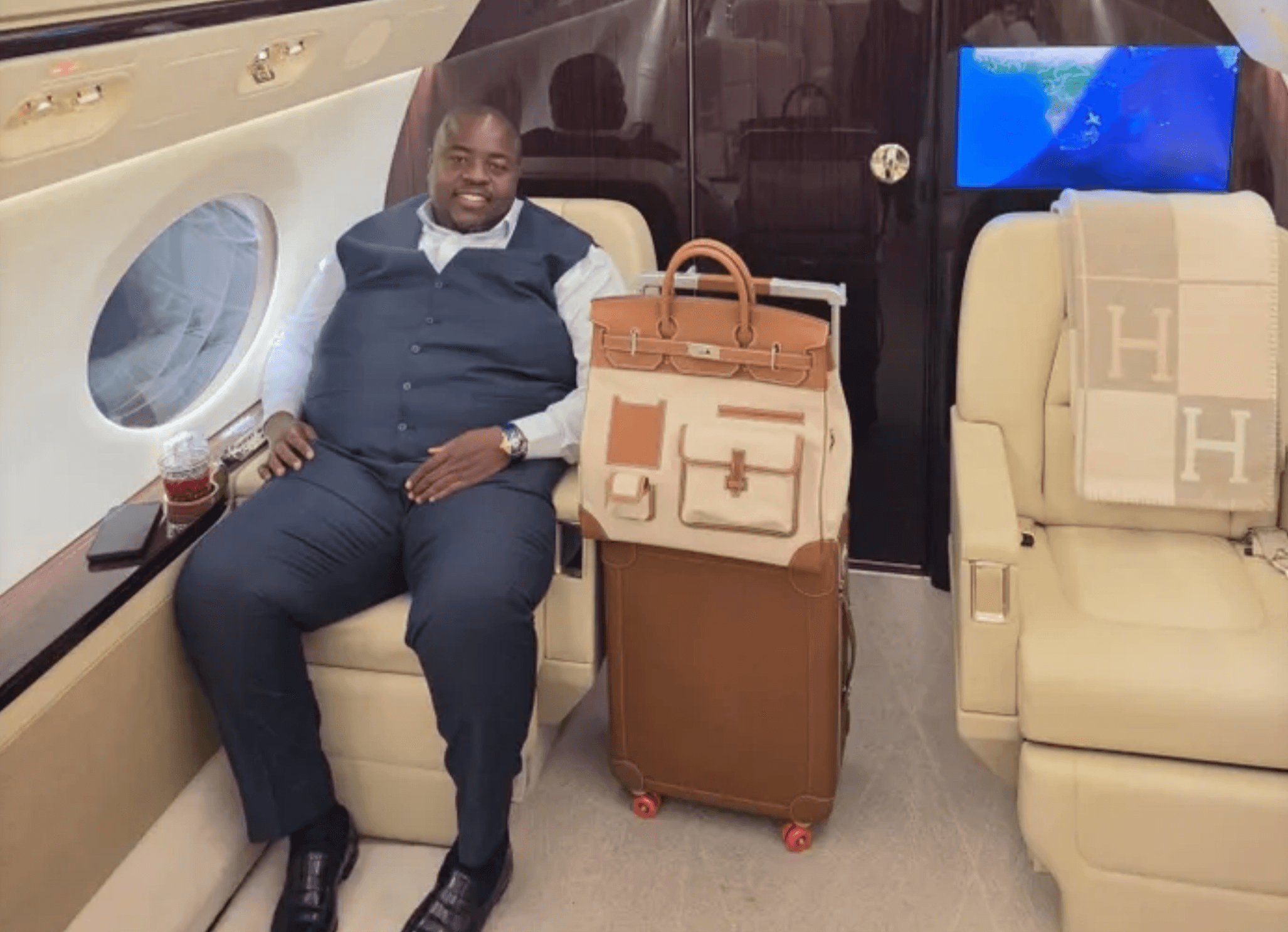 Wicknell Chivayo seated aboard a private jet beside a tan Hermès travel set