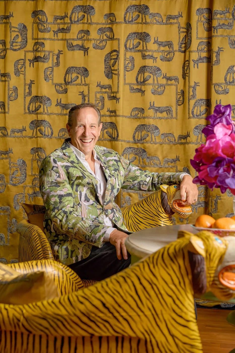 Bill Bensley smiling in a patterned jacket surrounded by tiger print furniture and a golden backdrop